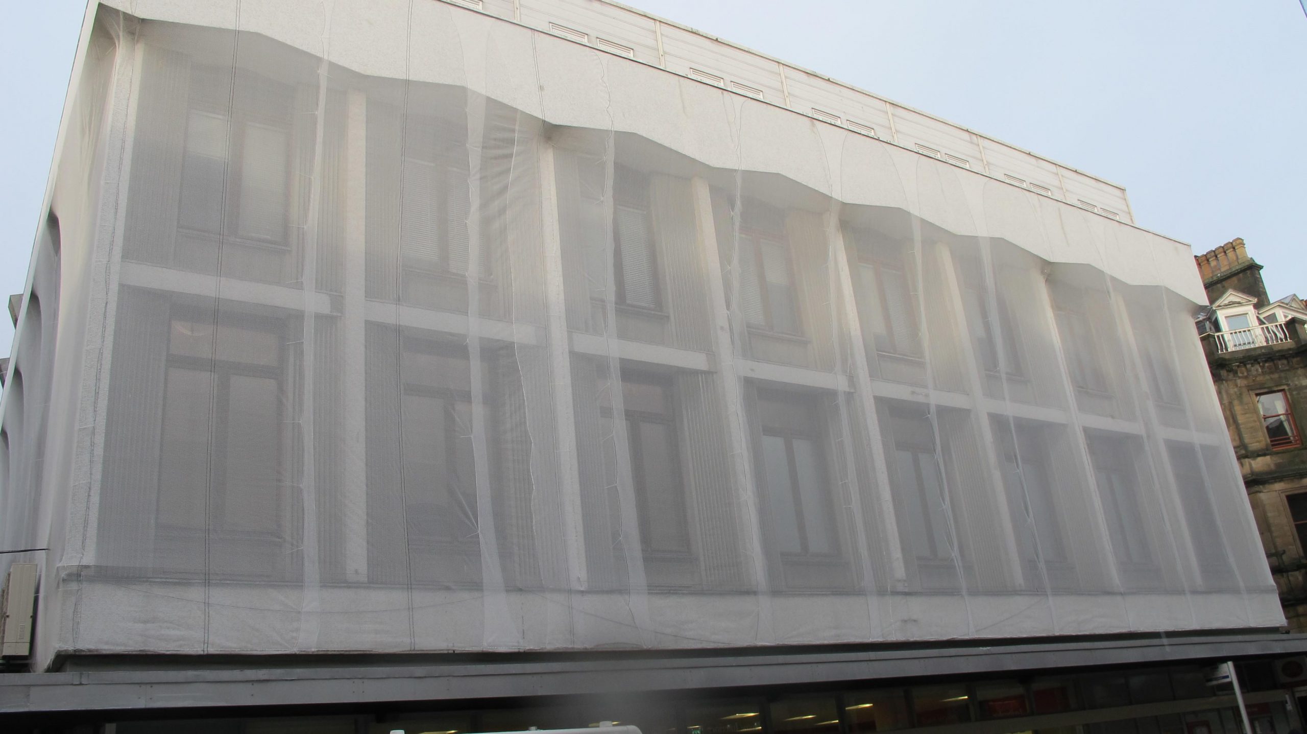 Building facade protected with fine mesh netting during height works